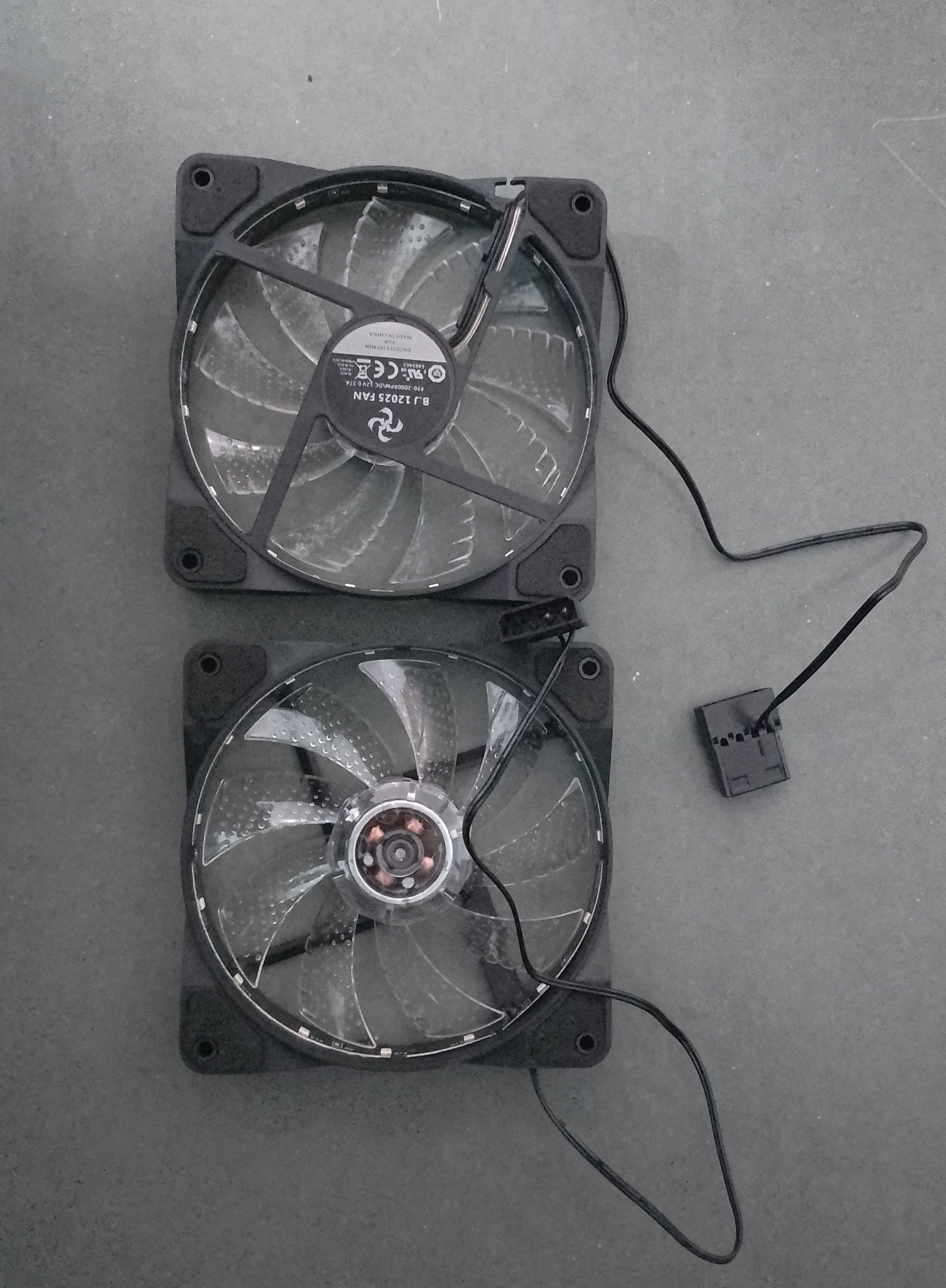 2 shitty case fans. The same model, but one of them is kept upside down. Sticker reads: B.J 12025 FAN 650-2000RPM\DC 12V 0.37A, followed by various safety/certification symbols, the part no., then RGB MADE IN CHINA. The connectors are MOLEX 8981 (the fat ones which connect to PSU outlets), with only 2 pins used. They have foam pads at the corners. The only redeemable quality is that the coil covering part is transparent and can be used for "educational" purposes.